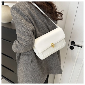 Détail d'un sac à bandoulière blanc avec fermoir doré sur une veste de blazer grise