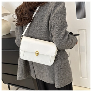 Petit sac blanc à bandoulière avec fermoir doré porté sur une veste grise