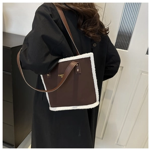 Detail view of brown leather bucket bag with white faux fur trim and gold logo on strap
