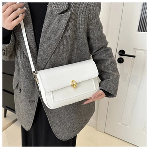 Détail du sac à bandoulière en cuir blanc avec fermoir doré sur blazer à chevrons