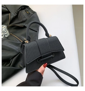 Detailed view of black woven texture handbag with gold hardware and trapezoidal structure