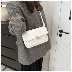 Gros plan d'un sac bandoulière blanc avec fermoir rotatif doré et bandoulière réglable