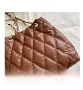 Close-up of brown quilted faux leather tote bag with glossy finish and gold metal chain