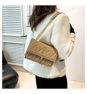 Detail of khaki square bag with geometric embossing and golden S-logo tassel charm