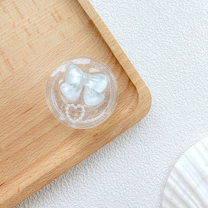 Detail of clear phone socket with white bow and pearl heart on a wooden tray