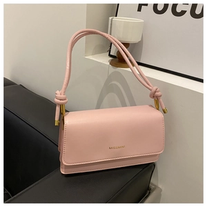 Detailansicht der rosa Umhängetasche mit Goldbuchstaben und Knotengurt auf Ledersofa