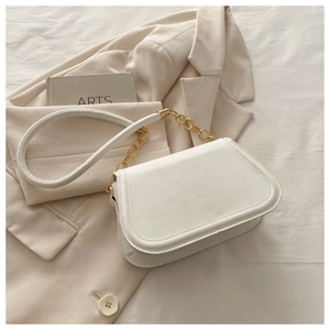 Detail of white shoulder bag with gold chain strap placed on a beige blazer jacket