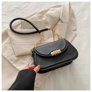 Detail of black matte leather bag featuring gold cylindrical clasp and metal chain strap