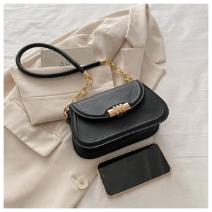 Detail of black leather bag featuring a gold cylindrical lock and chain shoulder strap