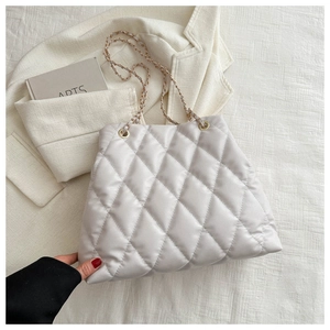 Detail of quilted rhombus texture and metal chain strap on light grey tote bag