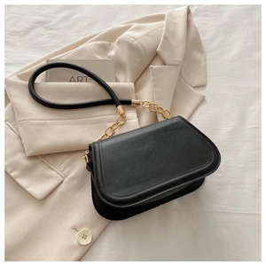 Close-up of black saddle bag with gold chain strap on beige blazer background