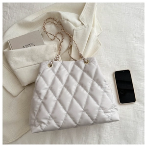 Close-up of ivory quilted tote bag featuring metal chain strap on textured fabric