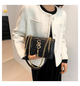 Detail of black quilted shoulder bag with gold chain strap and metallic tassel