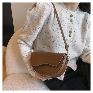 Gros plan d'une besace marron en cuir avec logo doré et fine bandoulière sur mannequin