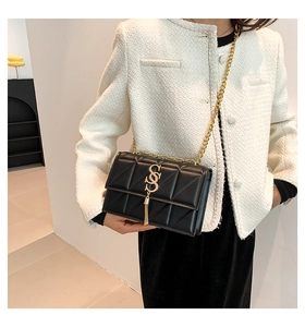 Detail of a black quilted chain bag featuring a gold double-S lock and tassel pendant