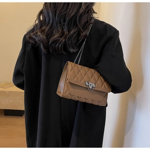 Dettaglio di una borsa trapuntata marrone con nappa in metallo su una modella