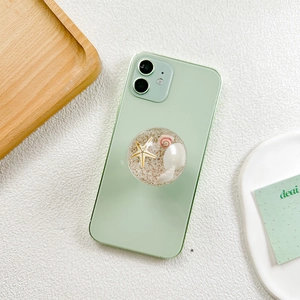 Macro detail of retractable phone grip featuring starfish and shells in sea sand