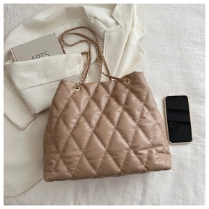 Close-up of brown quilted tote bag with golden chain strap on white knit fabric