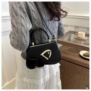 Detail of black leather saddle bag with gold metal buckle shown on a model's shoulder