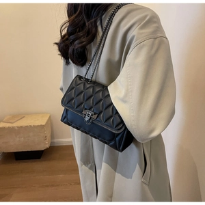 Dettaglio della borsa a tracolla trapuntata nera con catena indossata su un cappotto beige