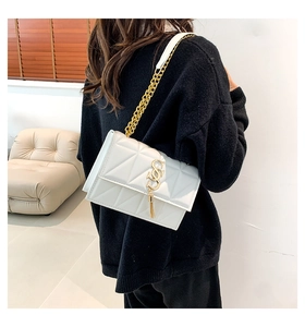 Detail shot of white quilted shoulder bag with gold chain strap and metal tassel charm