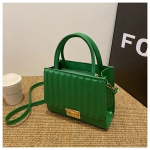 Détail du sac à main matelassé vert avec fermoir doré et bandoulière amovible sur tapis