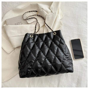 Detail of black quilted bucket bag with gold chain strap on a stylish white background