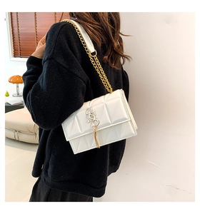 Detail of white quilted crossbody bag featuring gold chain strap and metallic tassel