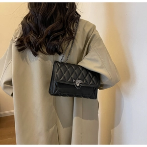 Dettaglio borsa a tracolla trapuntata nera con catena su un cappotto beige elegante