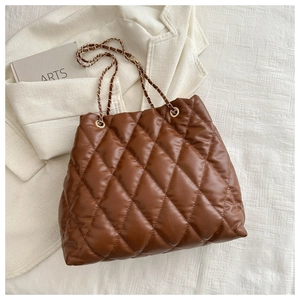 Top view of brown quilted tote bag with gold chain strap on a white blazer background