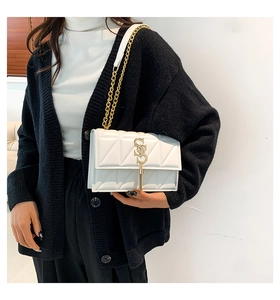 Close-up of a white quilted crossbody bag with gold chain and lettered metal hardware