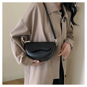 Détail d'un sac besace en cuir noir avec boucle dorée sur un trench-coat beige