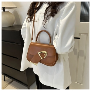 Detail of brown leather handbag with large gold D-ring buckle worn by model