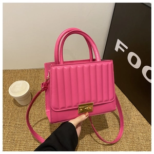 Detail of bright pink quilted leather bag with golden square lock and hand-held handle