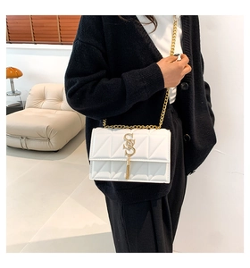 Detail of white quilted crossbody bag with golden SS metal logo and elegant tassel accents