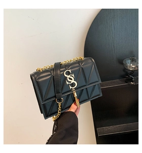 Detail of black quilted crossbody bag featuring a gold S-logo and fringe tassel charm