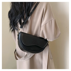 Vue détaillée d'un sac selle noir avec rabat ondulé porté sur un trench-coat beige clair