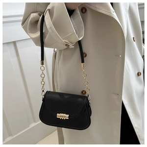 Close-up of black leather saddle bag with gold metal buckle and chain shoulder strap