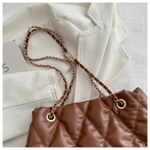 Detail of dark brown quilted bucket bag with gold chain strap on beige blazer