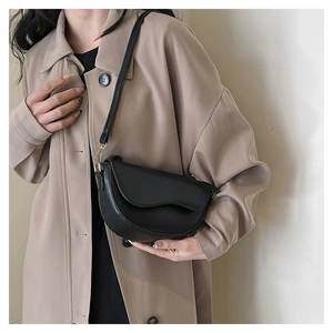 Détail d'un sac besace noir en cuir PU texturé avec rabat ondulé et boucles dorées