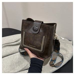 Detail of dark coffee vintage bucket bag with gold rivets and colorful geometric strap