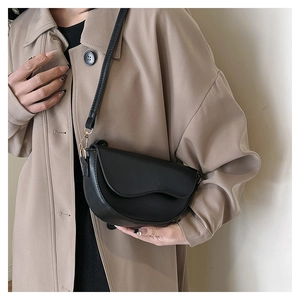Détail d'un sac besace noir minimaliste avec rabat ondulé et bandoulière fine