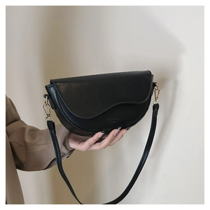 Détail du sac selle en cuir noir minimaliste avec bord ondulé et boucles dorées