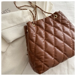 Detail of brown quilted bucket bag with golden hardware and leather chain strap on a magazine