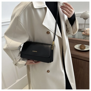 Detail der schwarzen Leder-Schultertasche mit goldenem Logo und weißem Trenchcoat