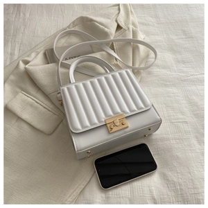 Détail du sac bandoulière blanc matelassé avec fermoir doré sur fond en tissu beige