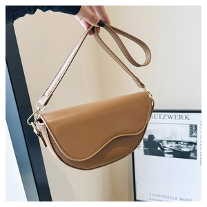 Détail d'un sac selle en cuir marron avec rabat incurvé et logo embossé à la main