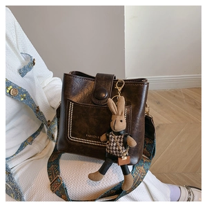 Detail of dark brown vintage bucket bag with patterned wide strap and rabbit charm