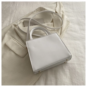 Détails d'un sac à main carré blanc avec poignée ronde et clous de fond en métal doré