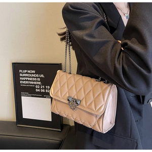 Dettaglio della borsa a tracolla trapuntata beige con catena in metallo indossata dal modello